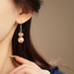 Detailed close-up of an elegant rose gold pearl earring worn by a model in warm light