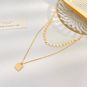Double-layered gold necklace with square pendant and disc charms on minimalist white background