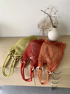 Three macrame woven shoulder bags in green, red, and orange with wooden ring handles