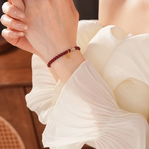 Detail of red bead bracelet with white stone and gold Fu character charm on wrist