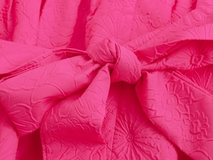 Macro shot of rose red jacquard fabric featuring a detailed embossed bow knot texture
