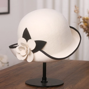 Detail of white wool felt cloche hat featuring black trim and 3D camellia flower accent