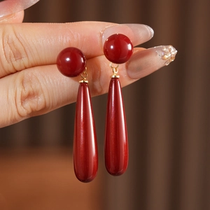 Detail view of vermilion teardrop earrings with golden rings held by a person's hand
