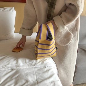 Detail showing hand holding a yellow and purple striped knitted tote bag on bed