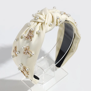 Detail of cream fabric headband with imitation pearls and white enamel bow accents