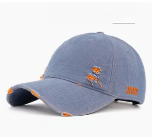 Close-up of distressed denim baseball cap with 1999 orange embroidery and ripped details