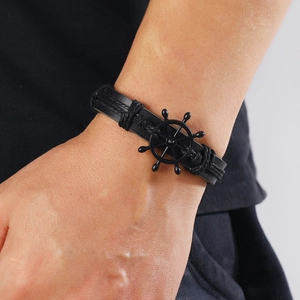 Close-up of black leather woven bracelet featuring a vintage metal ship helm charm