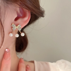 Dettaglio di orecchini a fiocco dorato con pavé di strass e tre perle pendenti fini