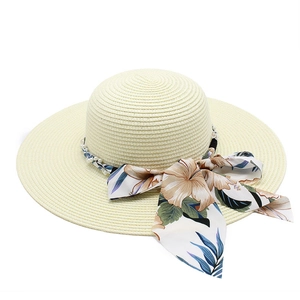 Close-up of beige straw sun hat featuring white pearl beads and floral ribbon bow detail