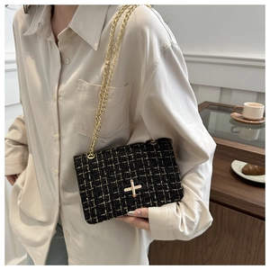 Detail of black tweed crossbody bag with gold chain strap and cross-shaped metal lock