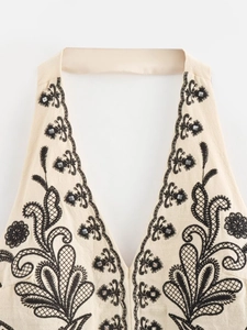 Detail of embroidered halter neckline with black lace trim and beaded accents on beige top