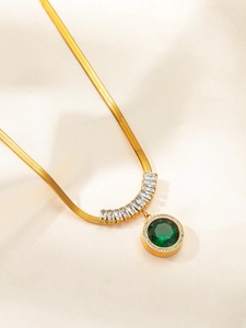 Detail of emerald green pendant on gold snake chain resting on soft beige silk fabric