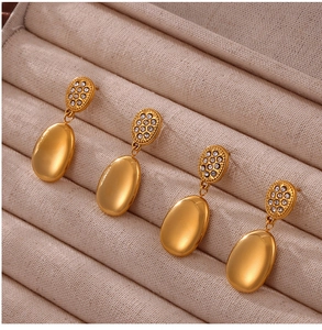 Macro shot of gold teardrop earrings featuring crystal-inlaid studs in beige jewelry box