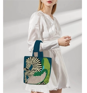 Deep blue bucket bag with zebra print and leaf pattern worn by a model in white dress