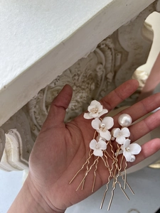 Detailed view of hand-held gold bridal hair pins with white ceramic flowers and pearls