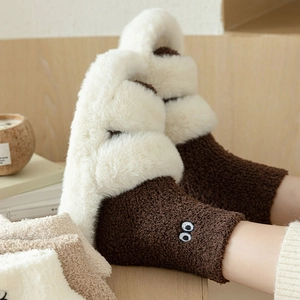 Close-up of plush coral fleece socks with cute eye embroidery in a cozy home setting