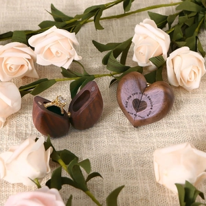 Macro shot of heart walnut ring box with engraved vows and decorative white roses