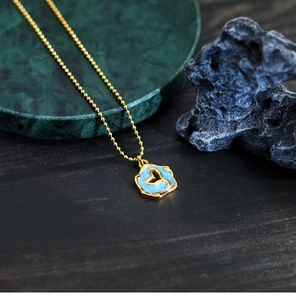 Macro shot of gold whale tail charm on sky blue enamel pendant with golden bead chain
