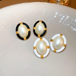 Close-up of vintage oval earrings with gold frames and faux pearl inlays in black and white