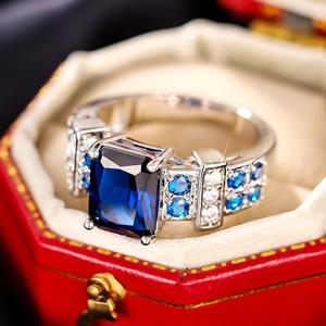 Macro shot of square blue sapphire ring with side diamonds in a red velvet jewelry box