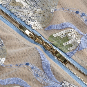 Detail eines goldenen Doppelreißverschlusses und Stickerei auf Pailletten-Netzkleid