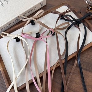 Five assorted colors of faux leather bow claw clips with long ribbons on a tray