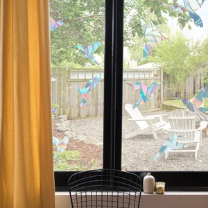 Detailed view of rainbow prism hummingbird window clings reflecting holographic light in garden