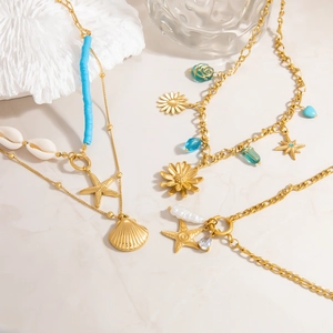 Close-up of golden starfish and seashell pendants on layered stainless steel necklaces