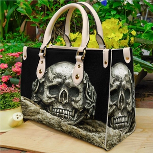 Gothic black PU leather shoulder bag with silver skull pattern shown in a garden setting