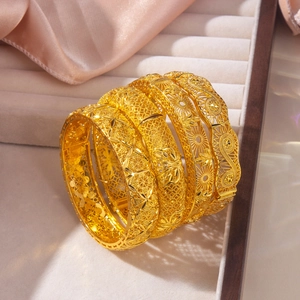 Detailed view of four gold-plated bangles with intricate hollow filigree flower patterns