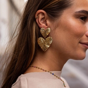 Close-up of golden double heart earrings with radial texture worn by a fashion model