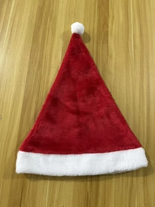 Flat lay view of a plush red and white Christmas hat on a light wood grain surface