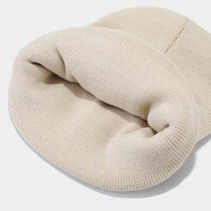 Detailed macro view of the ribbed knit texture on a cream-colored beanie cap