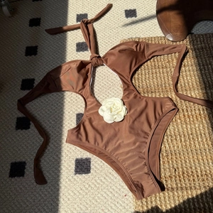 Detail of a brown halter swimsuit featuring a large 3D white flower and side cutouts