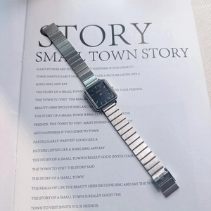 Macro detail of a minimalist rectangular quartz watch with silver steel chain band on a magazine