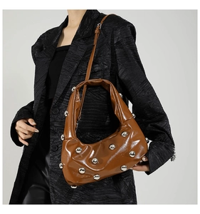 Detail of caramel glossy half-moon bag with silver metal rivets on a black blazer