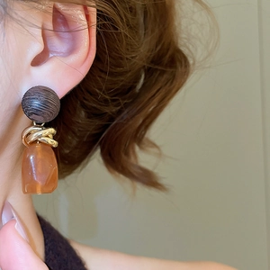 Détail de boucles d'oreilles géométriques en résine ambre et métal torsadé doré