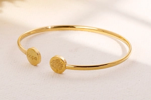 Close-up of golden open bangle featuring engraved Hope and Tree of Life charms