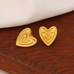 Detail of layered gold heart stud earrings with a polished finish on a wooden surface