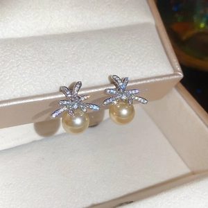 Detailed close-up of zircon flower earrings with golden pearl drops on a beige jewelry box