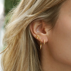 Detail view of gold snake earrings and geometric zircon hoops set on a model's ear