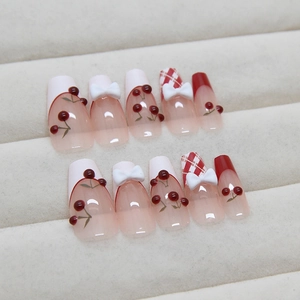 Unghie finte stile francese con ciliegia rossa, motivi a quadretti e fiocchi 3D