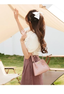 Detail of pink monogram handbag with metal lock and long strap shown in outdoor setting