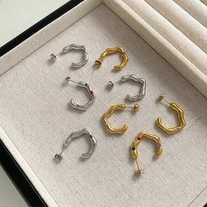 Golden and silver wavy C-shaped hoop earrings with colorful gemstones in a jewelry tray