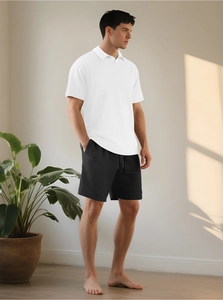 Dettaglio della trama della polo bianca e dei pantaloncini neri nel set estivo da uomo