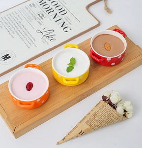 Three colorful ceramic heart ramekins with polka dots and handles on a wooden tray