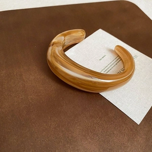 Detailansicht eines bernsteinfarbenen Acryl-Armreifs auf elegantem braunem Leder