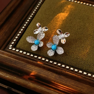 Detail of silver clover earrings with inlaid crystals and a turquoise center stone