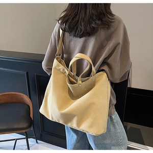 Detail of a large yellow canvas tote bag worn on shoulder by a model in a minimalist room