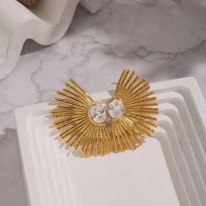 Détail de boucles d'oreilles soleil dorées avec grands zircons ovales sur fond de marbre